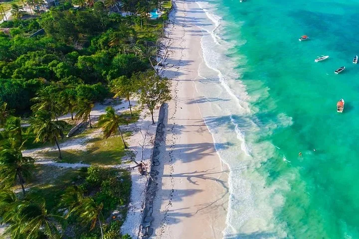 Luftaufnahme eines weißen Sandstrands mit Palmen und türkisfarbenem Meer mit Booten.